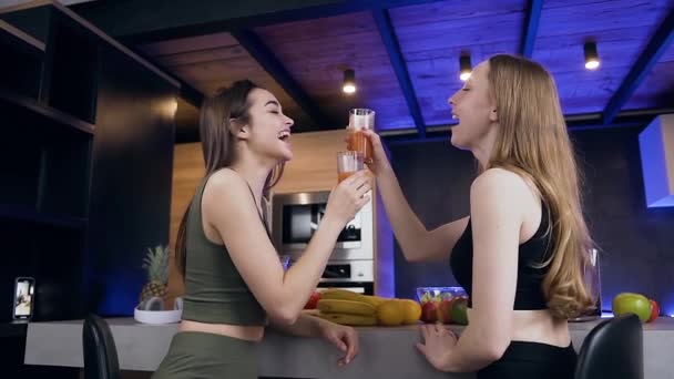 Close-up van charmante glimlachende jonge vrouwen die zitten in de buurt van de keukentafel en het drinken van vers sap — Stockvideo