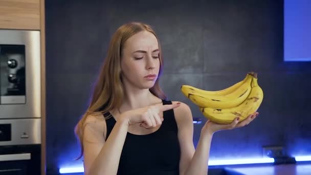 한 손에 바나나를 들고 싫어 하는 표시를 보이는 매력적 인 날씬 한 젊은 여자의 전경 — 비디오