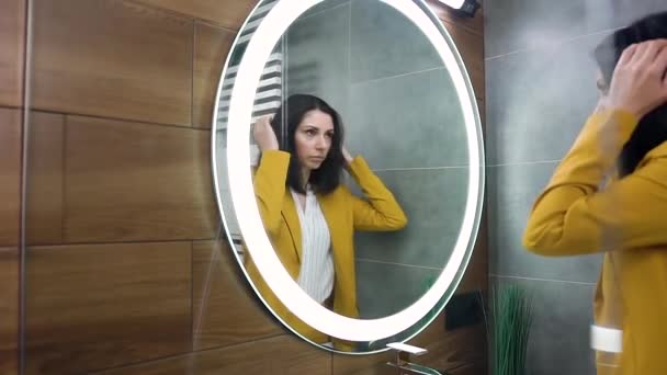 Великолепная серьезная молодая леди в деловом костюме, глядя на свое отражение в зеркале после одевания и укладки волос — стоковое видео