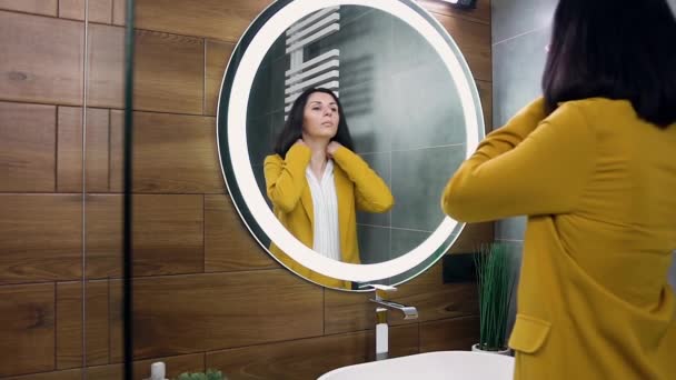 Attraktivt porträtt av självsäker 30-årig svarthårig affärskvinna i snygg kostym som står nära spegeln uträtning hennes kläder och frisyr — Stockvideo