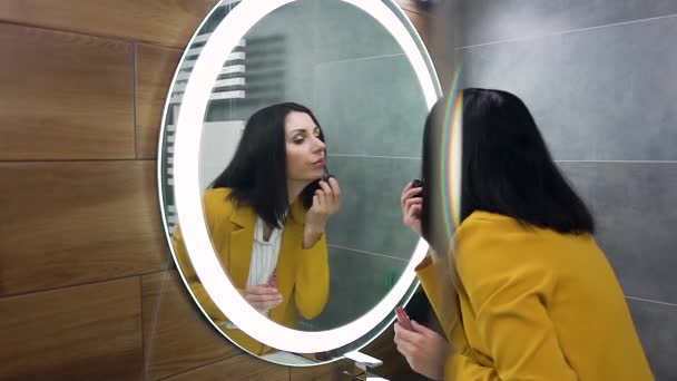 Cantik percaya diri wanita bisnis muda dalam setelan stylish menempatkan kemegahan di bibirnya sambil melihat ke cermin — Stok Video