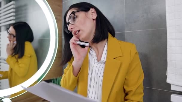 Närbild av snygg kreativ 30-årig svarthårig dam som står nära spegeln och talar på sin smartphone — Stockvideo