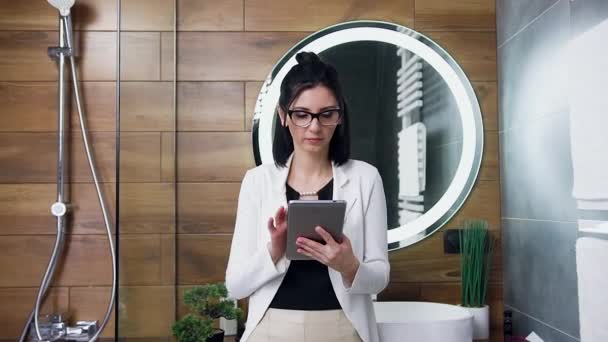 Confiado elegante morena con estilo en gafas vestidas con traje blanco trabajando en la tableta de la PC cerca del espejo de los baños — Vídeo de stock