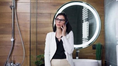 Banyosunda telefon görüşmesi yapan beyaz takım elbiseli, çekici, modern bir bayanı yakından çek.