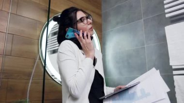 Banyoda iş ortağıyla telefonda konuşan 30 yaşında çekici bir iş kadınının portresi.