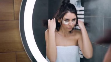 Vücudunun etrafında havluyla kendine güvenen güzel bir esmer aynaya bakıyor ve göz altında yamaları inceliyor.