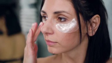 35 yaşında fevkalade bir esmerin yan görünüşü. Aynaya bakıyor ve gözlerinin altındaki pürüzleri gideriyor.