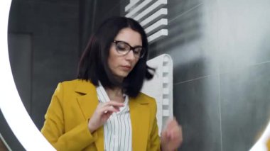 Banyodan çıkmadan önce aynada kendine bakan genç, çekici, siyah saçlı bir iş kadını.