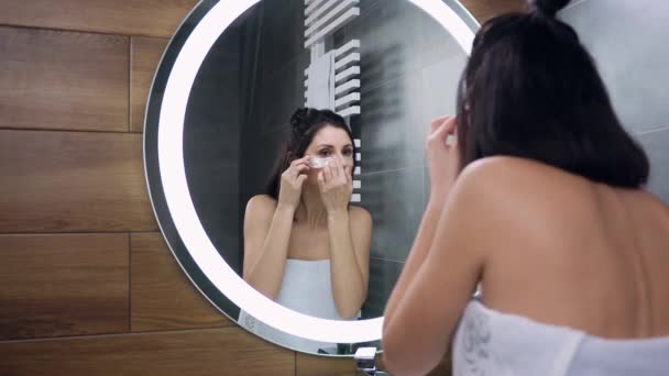 Pohled zezadu roztomilé černošky vlasy žena v bílém ručníku kolem jejího těla, který dává skvrny pod očima pro svěží vzhled — Stock video