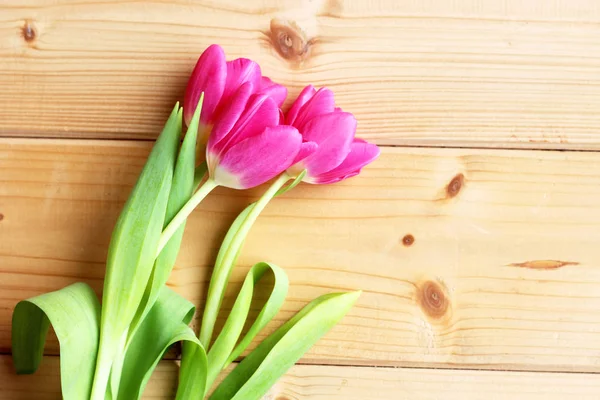 Top view of pink tulips arranged in line over wood background. Spring greetings card with tulips for Easter, Mothers Day. Copy space.