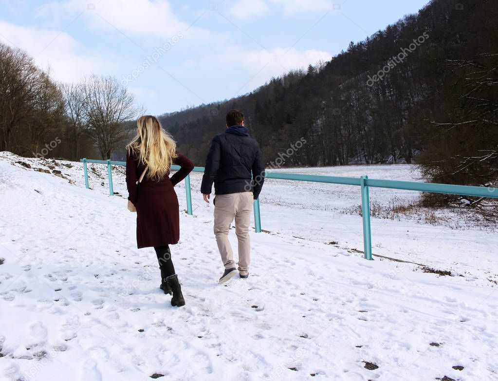 A beautiful couple walking on a snowy road in the woods .People, season and leisure.