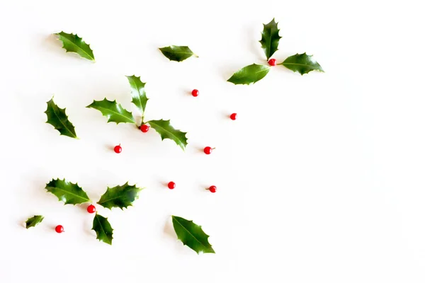 Navidad acebo Ilex aquifolium aislado sobre fondo de mesa blanca. Hojas de hoja perenne con bayas rojas. Marco floral decorativo, banner web. Asiento plano, vista superior. Espacio vacío para texto de vacaciones . Fotos De Stock