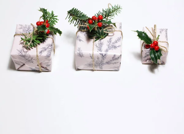 Horní pohled na bílou dárkovou krabici svázaná a zdobená cesmínovou větvičkou na bílém dřevěném pozadí.Vánoční koncept. — Stock fotografie