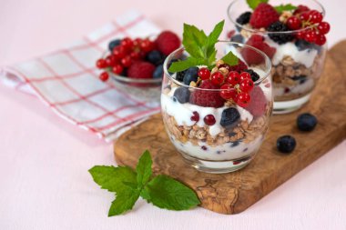 Yoğurtlu, ahududulu, yaban mersinli ve pembe fonda kırmızı frenk üzümlü granola parfe..