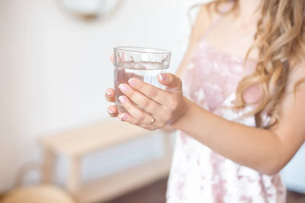 A női kezek egy tiszta pohár vizet tartanak. Nyálas test a háttérben. Egészséges életmód. — Stock Fotó