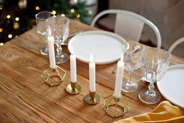 Masa, oturma odasında bir Noel yemeği için servis ediliyor, yakın görüş, masa örtüsü, beyaz tabaklar, çatallar, bıçaklar, şarap için bardaklar, altın şamdanlar içinde mumlar, Noel.