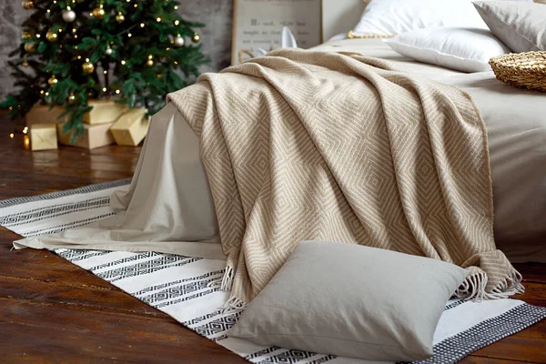 Arredo appartamento di Natale, scandinavo accogliente arredamento domestico, letto con calde coperte a maglia accanto all'albero di Natale. Luci e ghirlande . — Foto Stock