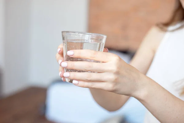 Mãos femininas segurando um copo transparente de água.Um copo de água mineral limpa nas mãos, bebida saudável . — Fotografia de Stock