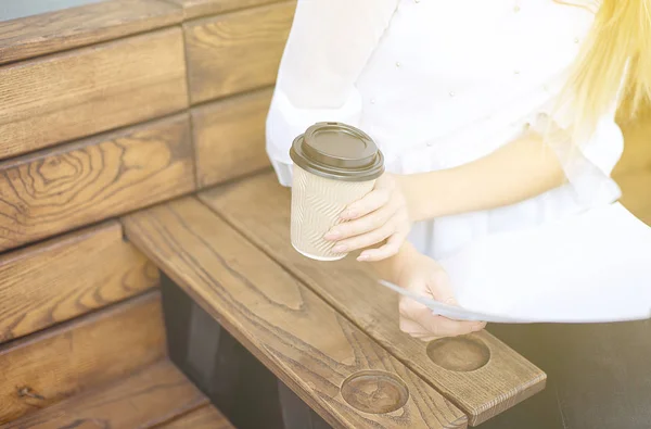 Junges Mädchen hält auf einem Street-Food-Festival eine Tasse Kaffee oder Tee aus Papier auf einem Holztisch in der Hand. — Stockfoto