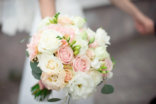 Gros plan marié dans un costume et la mariée dans une robe blanche sont debout et tenant un bouquet de roses pêche, eustomes et fleurs et de verdure — Photo