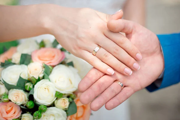 Le mani degli sposi sposi sposano con fedi nuziali d'oro primo piano su uno sfondo di un mazzo nuziale di rose — Foto Stock