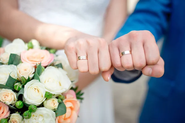 Le mani degli sposi sposi sposano con fedi nuziali d'oro primo piano su uno sfondo di un mazzo nuziale di rose — Foto Stock