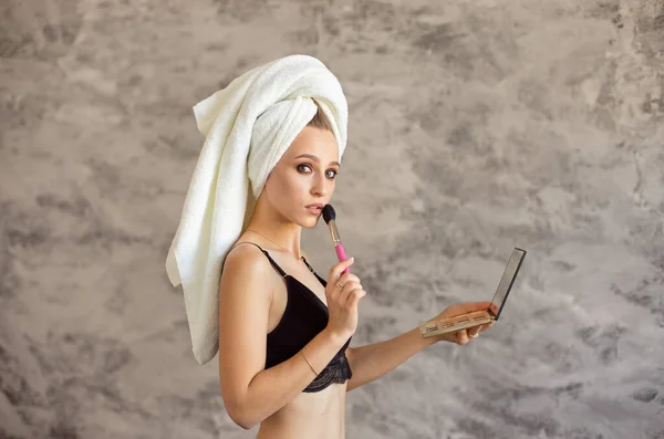 Maquillaje de una niña, una joven hermosa con una toalla blanca, cabello después del lavado, se aplica maquillaje, se aplica rubor en los pómulos en la mañana . —  Fotos de Stock