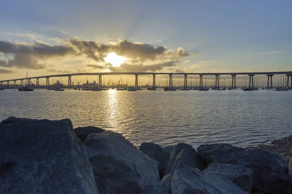 Rocks and puffy clouds frame the early morning sun and the Coronado Bridge — Stock Photo, Image