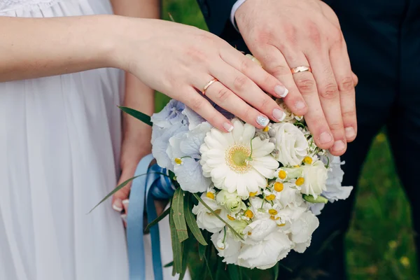 Mãos e anéis no buquê de casamento — Fotografia de Stock