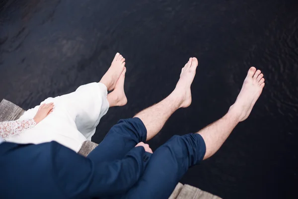 Las piernas de la novia y el novio en un vestido de novia zapatos en el agua de mar. Fondo de verano — Foto de Stock