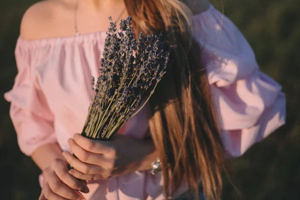 Schöne junge Frau mit einem Lavendelstrauß und träumt in den Sonnenuntergangsstrahlen — Stockfoto