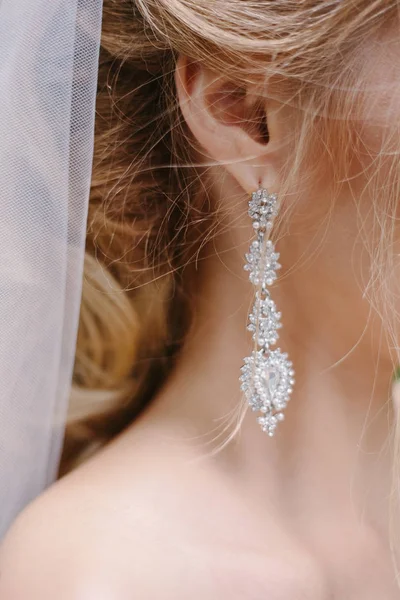 Wedding preparation. Beautiful, happy bride dresses earrings before wedding.