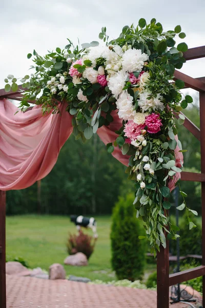 Arch for the wedding ceremony. Arch, decorated with beautiful fresh flowers and cloth. Bordeaux color. Registration at the place of marriage.