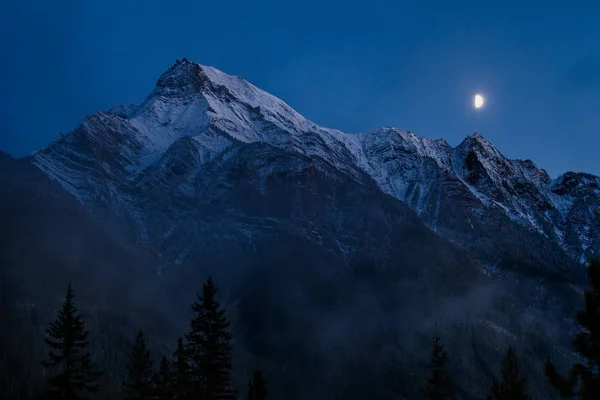 Луна поднимается над снежной горной цепью в туманный вечер — стоковое фото