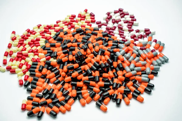 Orange, black, grey, white, red, pale yellow antibiotic capsule pills on white background. Drug resistance concept. — Stock Photo, Image