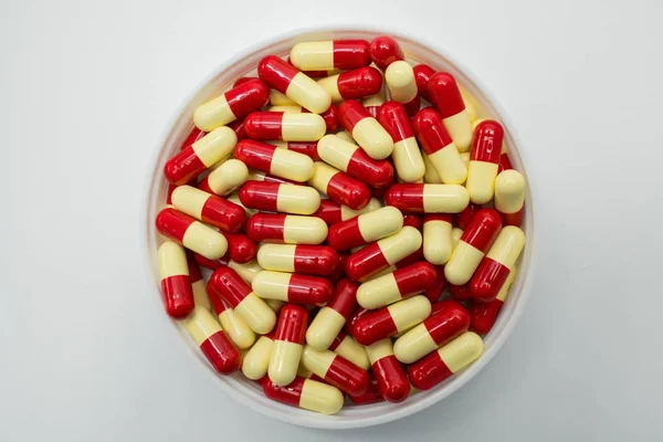 Top view of red, pale yellow, capsule pills in plastic container on white background — Stock Photo, Image