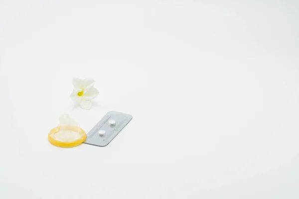 Pílulas contraceptivas de emergência com preservativo e flor no fundo branco — Fotografia de Stock