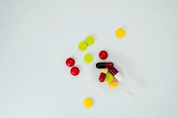 Comprimidos coloridos em colher de chá e muitas pílulas espalhadas em um fundo branco com espaço de cópia — Fotografia de Stock
