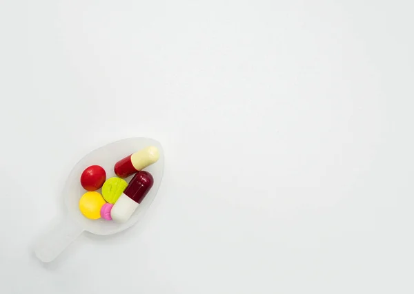 Pilules colorées dans une cuillère à café sur fond blanc avec espace de copie — Photo