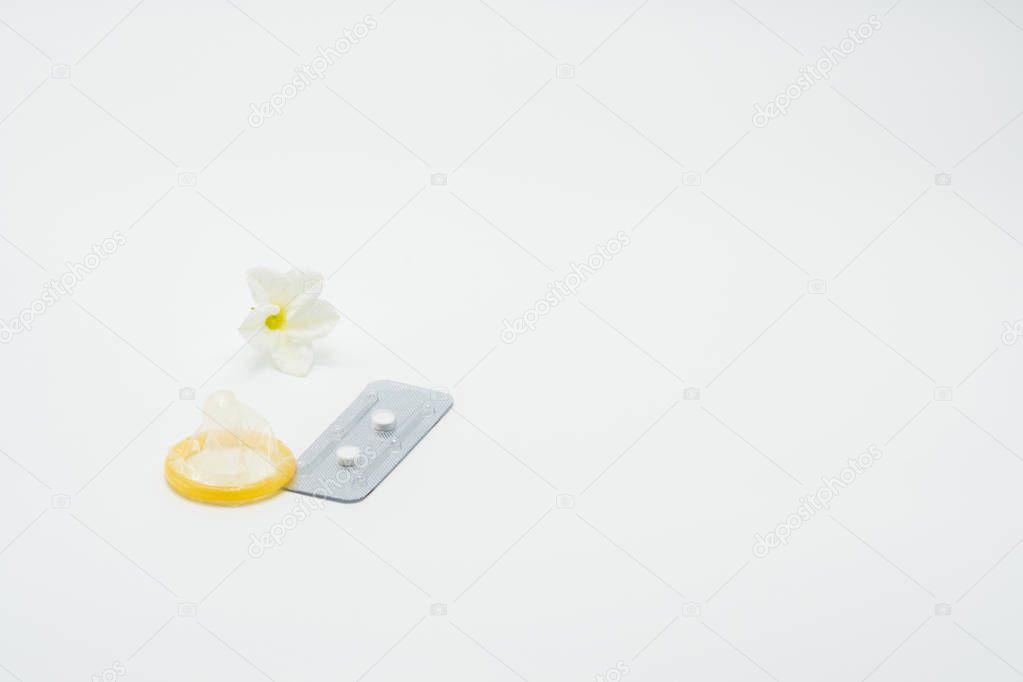 Emergency contraceptive pills with condom and flower on white background