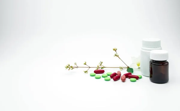 Röd, grön tillägg och vitamin tablett och kapsel piller med blomma och gren med Tom etikett plast, bärnstensfärgad glasflaska på vit bakgrund med kopia utrymme, bara lägga till din egen text — Stockfoto