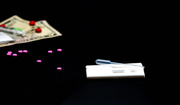 Dois testes de cassete de metanfetamina e conta-gotas de plástico com drogas rosa, notas de dólar americano e seringa como fundo escuro desfocado com espaço de cópia — Fotografia de Stock