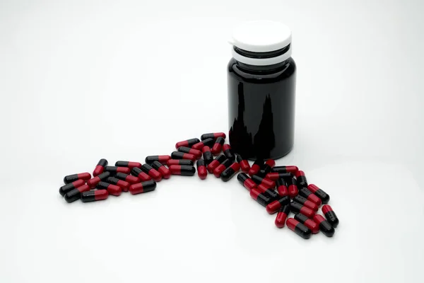 Rood, zwarte antibiotica capsule pillen en bruine plastic fles geïsoleerd op een witte achtergrond met kopie ruimte, drug weerstand concept — Stockfoto