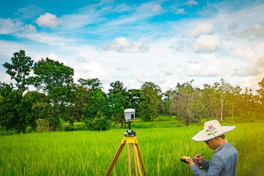 UBONRATCHATHANI, THAILAND-SEPTEMBER 26, 2017 : Asian smart engineer or surveyor is working on controller screen for surveying land in rice field. GPS surveying instrument. clipart