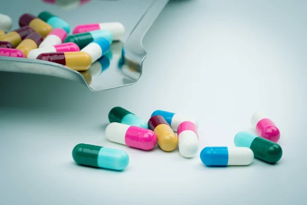 Bunte Tabletten mit Antibiotika-Kapseln auf Edelstahl-Medikamententablett und einige davon auf weißem Hintergrund, Arzneimittelresistenzkonzept. — Stockfoto