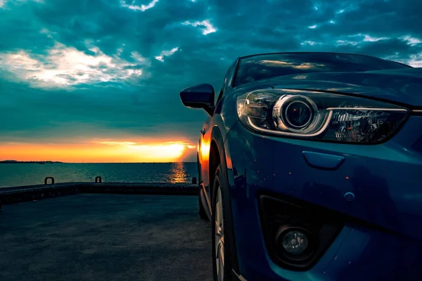 Carro SUV compacto azul com esporte e design moderno estacionado na estrada de concreto junto ao mar ao pôr do sol. Tecnologia amiga do ambiente. Conceito de sucesso empresarial . — Fotografia de Stock