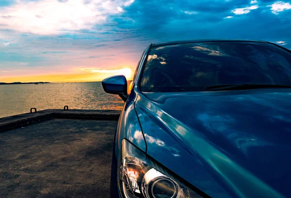 Μπλε συμπαγές Suv αυτοκίνητο με σπορ και μοντέρνα σχεδίαση παρκαρισμένο στο τσιμεντένιο δρόμο δίπλα στη θάλασσα στο ηλιοβασίλεμα. Φιλικό προς το περιβάλλον τεχνολογία. Επιτυχία της επιχειρηματικής ιδέας. — Φωτογραφία Αρχείου