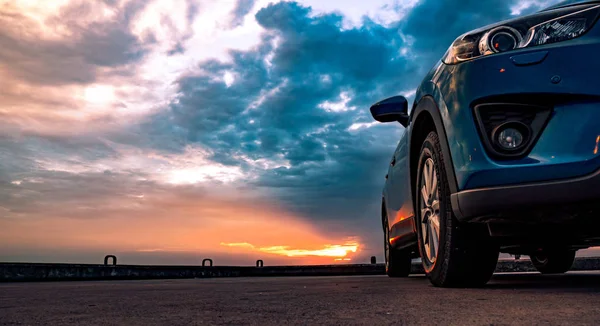 Voiture SUV compacte bleue au design sportif et moderne garée sur une route bétonnée au bord de la mer au coucher du soleil. Technologie respectueuse de l'environnement. Concept de réussite commerciale . — Photo