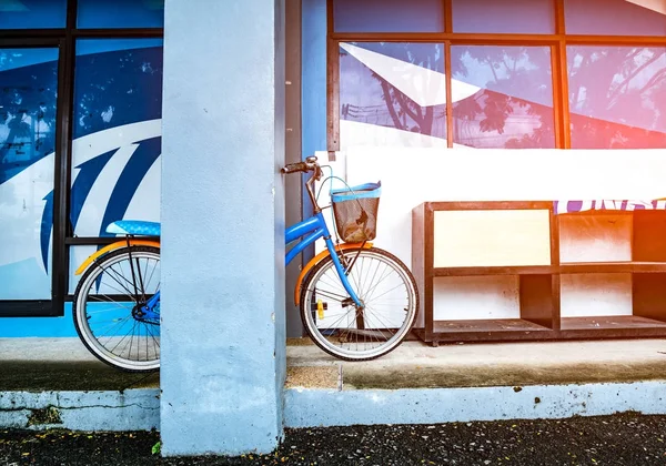 Bicicleta apoiada em um poste perto de um rack de sapato de madeira colocado em um piso de cimento em um edifício com luz flamejante. Estilo vintage . — Fotografia de Stock