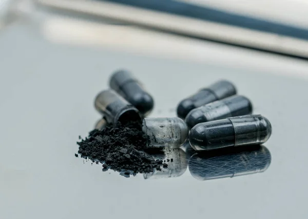 Selective focus on powders of activated charcoal on stainless steel drug tray and blur capsule background — Stock Photo, Image